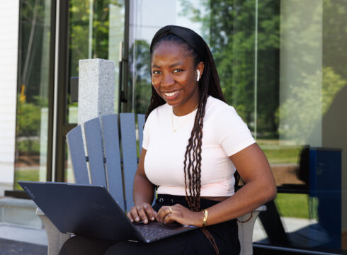 A female executive MBA student works on her laptop on a beautiful summer day at New England College during the summer 2024 residency.